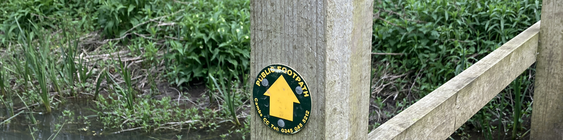 Photograph of a footbridge across a chalk stream with a public footpath sign attached