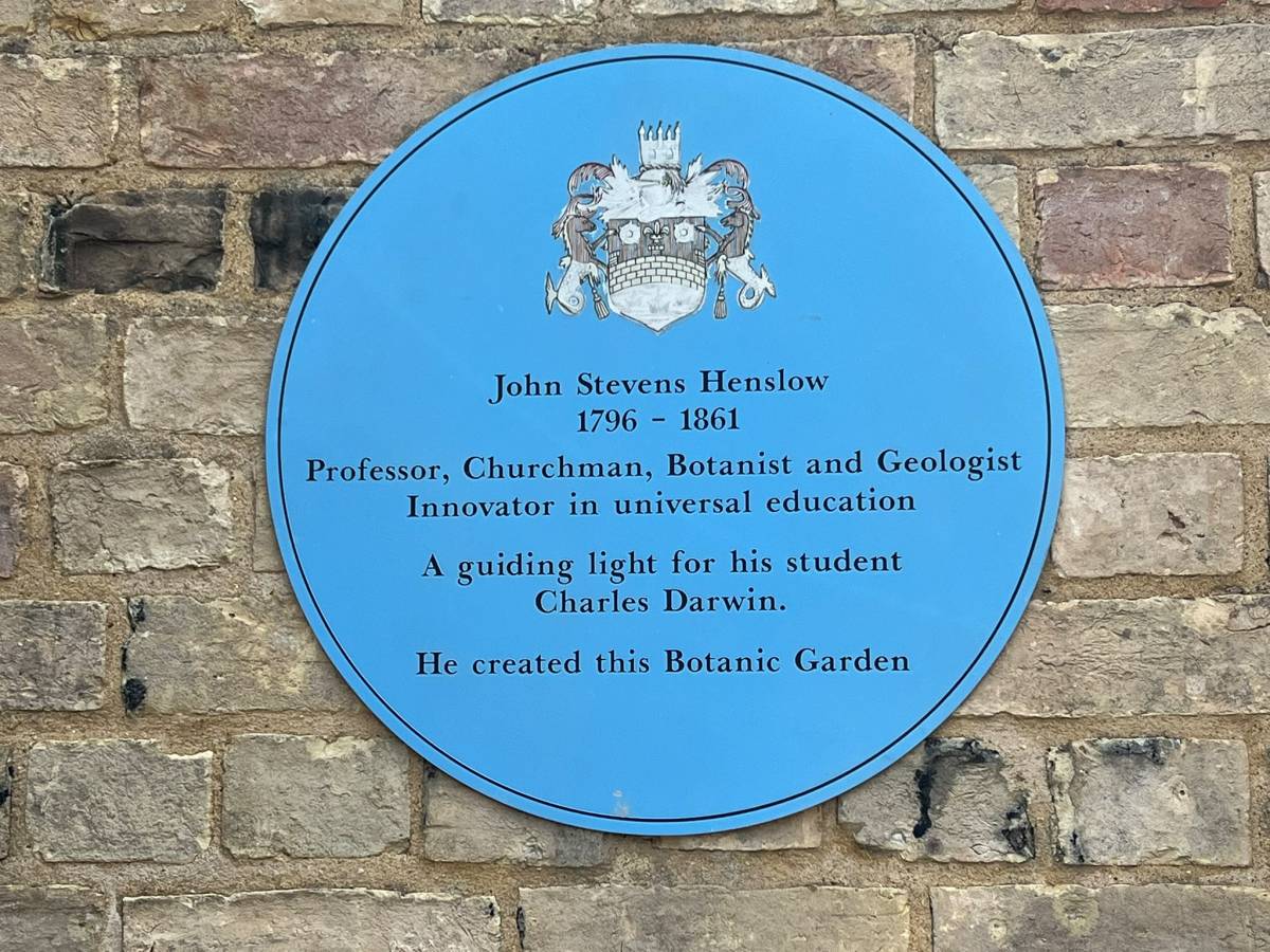 Photograph of the blue plaque to John Stevens Henslow in the Botanic Garden. The inscription reads "Professor, Churchman, Botanist and Geologist. Innovator in universal education. A guiding light for his student Charles Darwin".