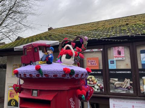 A photograph of a knitted post box topper at Foxton Shop featuring Postman Pat and his red van